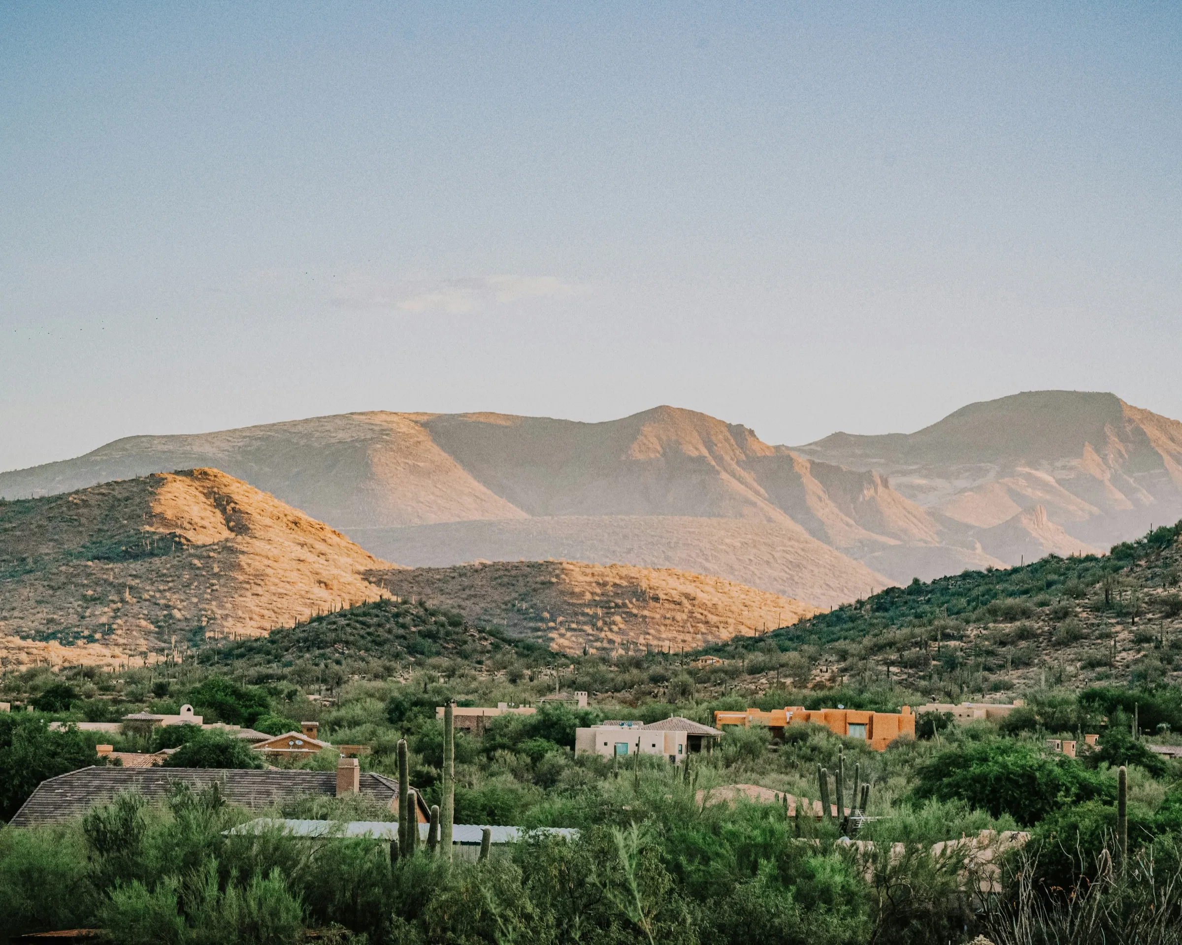 Desert foothills outside Tucson at dusk, with adobe homes and saguaros beneath the mountains