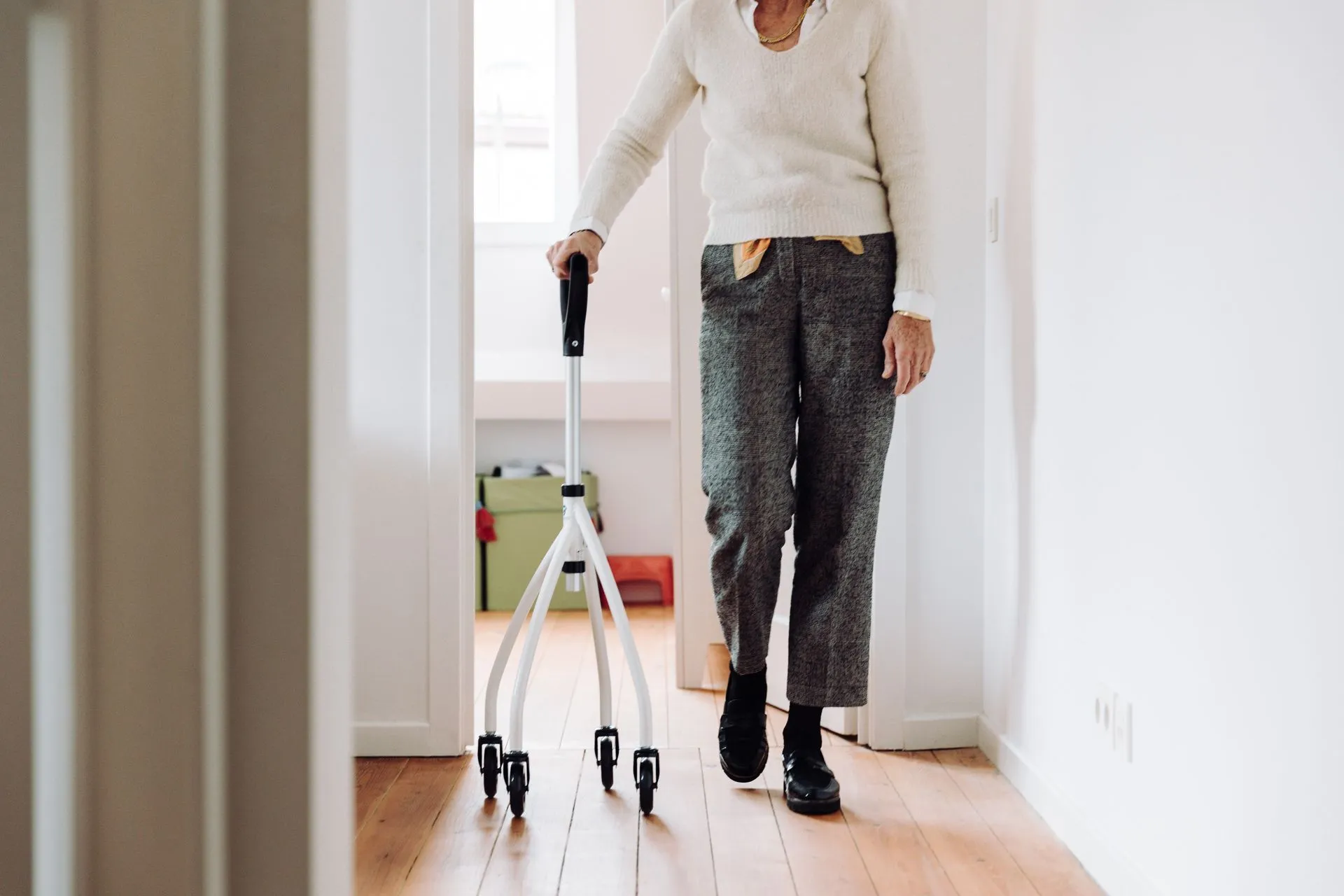 An older woman walking down a hallway at home with a wheeled walking cane