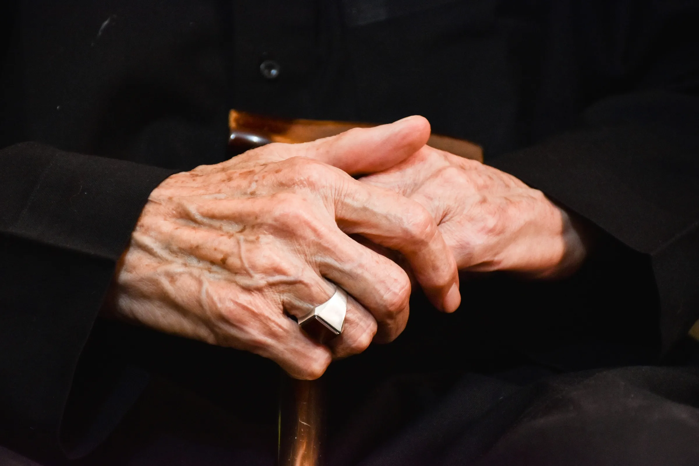 An older adult's hands resting together on the handle of a walking cane
